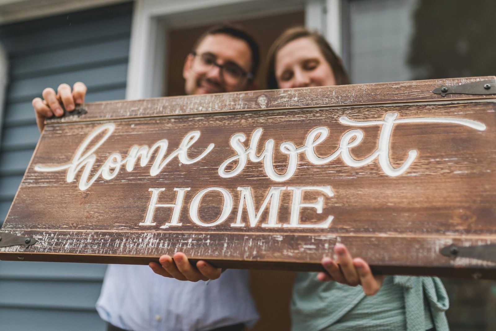 A joyful couple holding a 'home sweet home' sign in front of their new house.